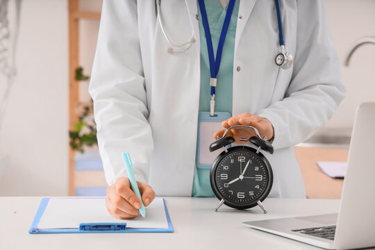 Female doctor with clipboard turning off alarm clock at desk in clinic