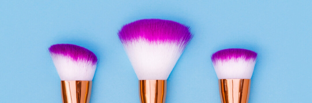 Brushes with purple tips on a blue background for makeup application and beauty routines