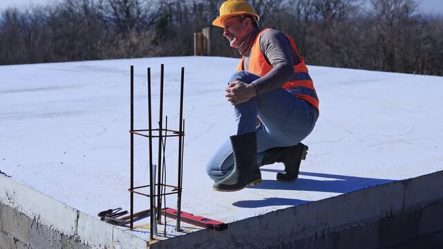 Construction worker having a accident and injured knee and leg on a construction site outdoors.
