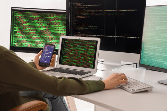 Female programmer working with mobile phone and computer at desk in office