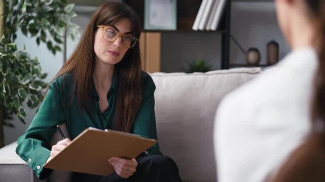 Video of female psychologist giving therapy to a patient while taking notes, sitting on the couch in the psychology office