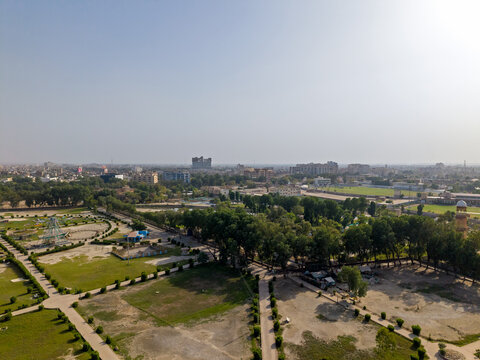 Aerial view of a lush green park with walking paths and amusement rides under a clear sky in Hyderabad, Sindh, Pakistan.