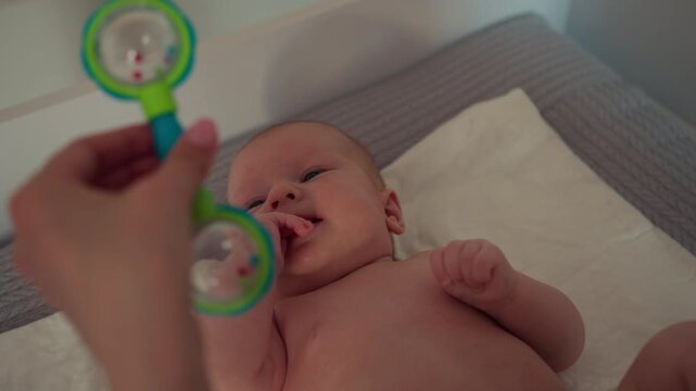 Parent s hand holding colorful rattle toy near infant s face, stimulating senses and interaction. The playful moment conveys discovery, happiness and the warmth of family care