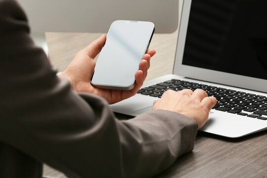 Young female programmer with mobile phone and laptop working in office, closeup