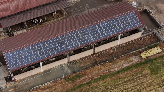 Farm Rooftop Solar Power: An aerial view of a farm building with a dark brown roof covered in solar panels, showcasing sustainable energy integration in an agricultural setting.