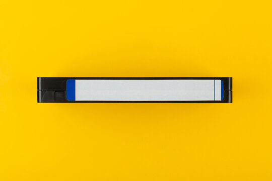 Side view of a black VHS cassette with a blank label on a vibrant yellow back