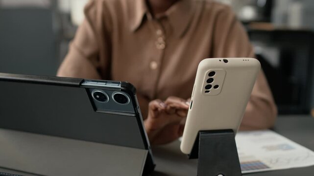Low angle close up tilt up shot of African American woman using both smatphone and digital tablet while working with documents in office