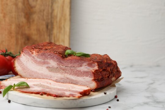 Pieces of smoked bacon, tomatoes and spices on white marble table, closeup. Space for text