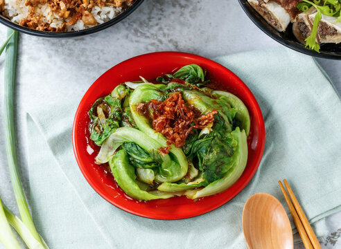 Delicious stirfried bok choy with crispy fried shallots on a red plate atop a table