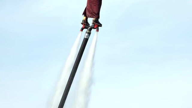 Flyboarding athlete flying with water jet pack over clear blue sky