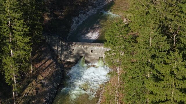 Aerial view revealing a mountain dam and rushing river behind pine trees, Austria