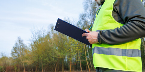 Close up male writing a report for a new construction project on a site after forest clearing. An ecologist conducts environmental monitoring and soil analysis. © A Stock Studio