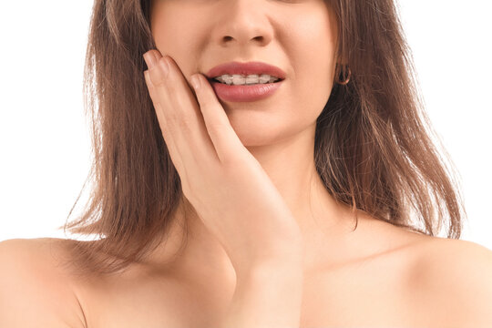 Young woman with dental braces suffering from toothache on white background, closeup