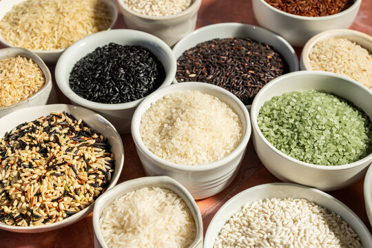 A variety of rice in white ceramic bowls on a tile surface 