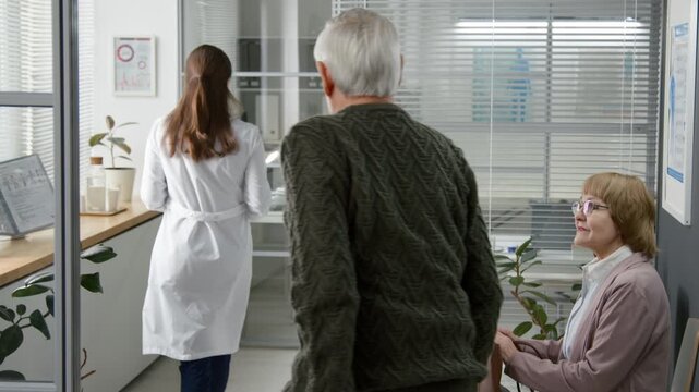 Elderly man following female doctor to consultation room while another patient waiting in queue at modern clinic