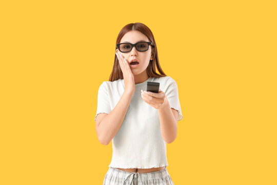 Shocked teenage Asian girl in 3D glasses watching cartoons on yellow background