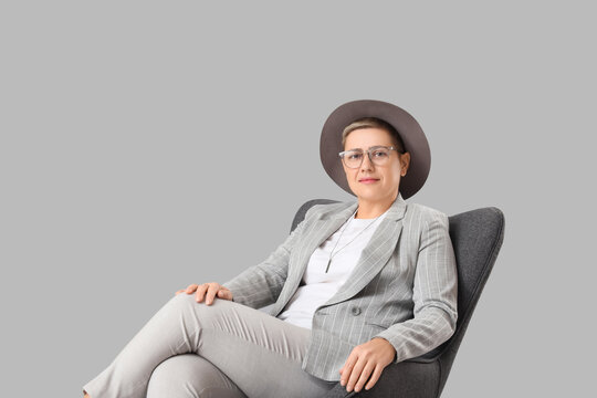 Stylish businesswoman with short hair sitting in armchair on grey background