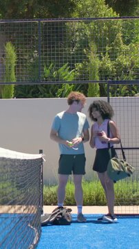 Vertical video: Picking paddles, ball, man embracing partner in sport kit on blue court after match
