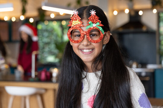 Indian family celebrating in kitchen with child wearing glittery tree glasses and patched sweater