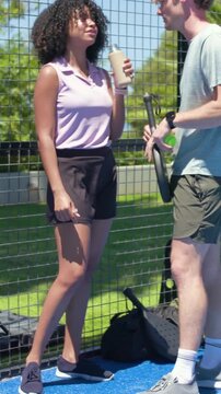 Vertical video: Sipping woman in pink top with bottle on court during break as man offering ball