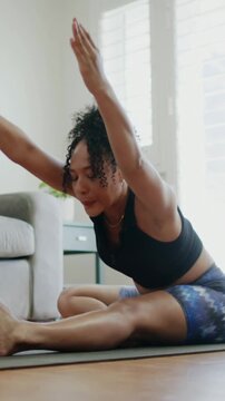 Vertical video: Exhaling woman in workout clothes folding on yoga mat at home, deepening stretch