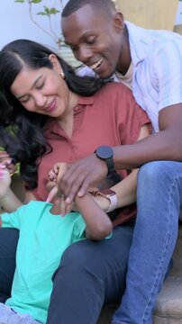 Vertical video: Sliding dad tickling child in green tee on steps, mom holding for fun, plants