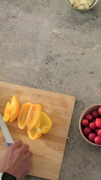 Vertical video: Removing core, cook's hands slicing yellow pepper on cutting board, prepping salad