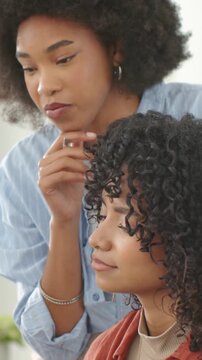 Vertical video: Leaning stylist blue shirt checking client's tight curls at salon, showing options