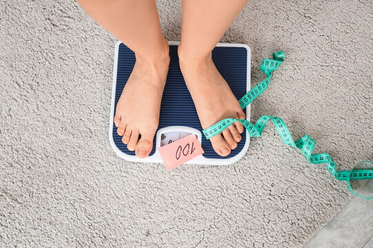 Woman's feet with tape measure and large number on weight scales at home, top view. Anorexia concept