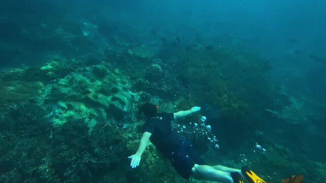 Freediver gliding above vibrant coral reef with yellow fins slow graceful descent across coral plates reveals reef topology, clear turquoise water, calm bubbles and peaceful, Amed,Bali