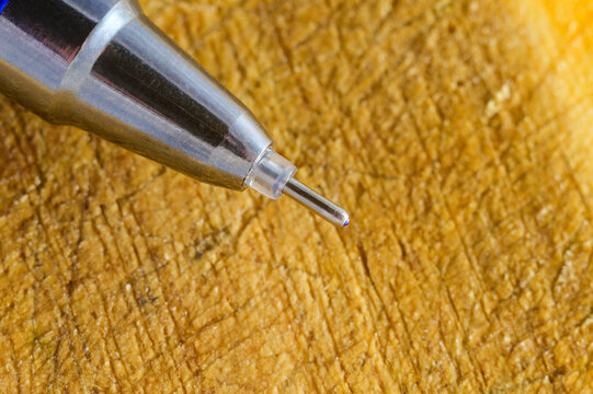 Close-up macro shot of a ballpoint pen tip resting on a textured wooden surface