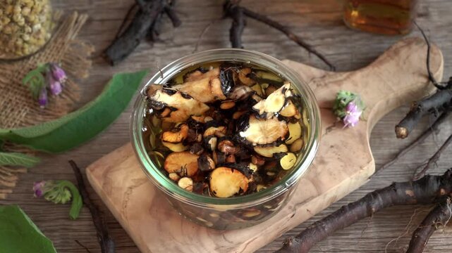 Pouring sliced comfrey or knitbone root into a jar with alcohol - preparation of homemade herbal tincture for bones