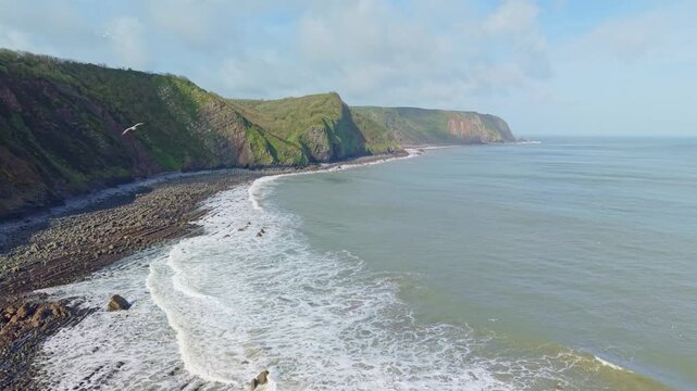 Aerial view of Mouthmill Beach which is a secluded pebble cove near Clovelly, North Devon, known for the dramatic Blackchurch Rock sea arch and waterfall. Ambient exploration by drone. 