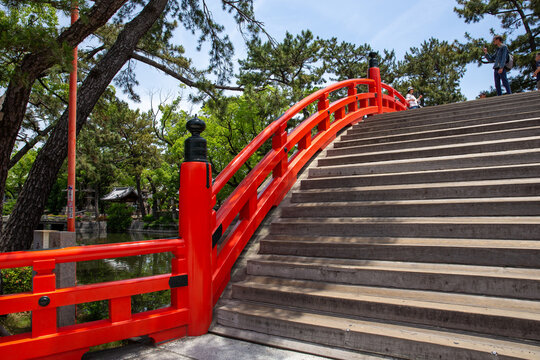 Rote japanische Bogenbr&uuml;cke mit Holzstufen und Gel&auml;nder in gr&uuml;nem Park mit Kiefern