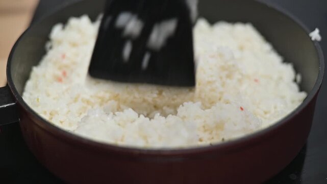 Rice is being stirred in a black pan on a stovetop. The activity showcases a cooking technique aimed at achieving the right texture for meals