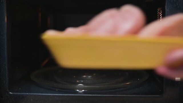 Chicken pieces are placed in a yellow dish and heated in a microwave. Hands are shown carefully adjusting the dish to ensure even cooking during the process