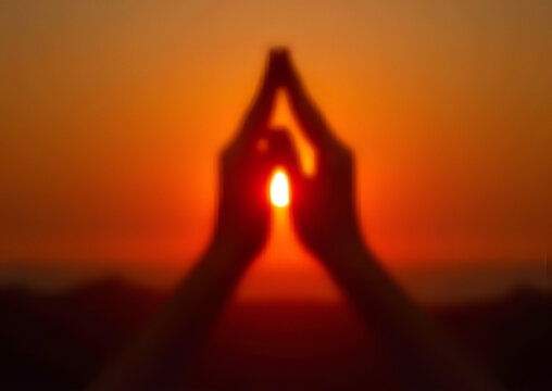 Silhouette of Blurred Hands in Prayer Position Framing Glowing Sun at Sunset