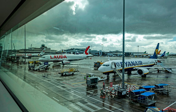 Malta Air, Lauda Europe, and Ryanair aircraft on a wet apron at Dublin Airport, Ireland, under a dramatic dark sky with ground crew in high-vis.