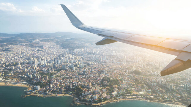 Airplane wing capturing a vibrant coastal city from above, showing urban buildings, ocean, and skyline under bright sunlight