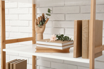 Wooden hand with books, flower and eucalyptus on shelf near white brick wall © Pixel-Shot