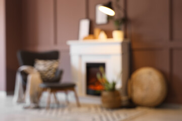 Obraz premium Blurred view of cozy living room with grey armchair, footstool, glowing lamp and stylish fireplace