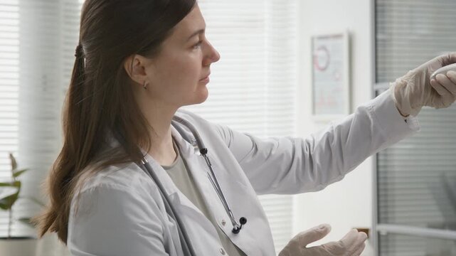 Medium handheld shot of young adult female general practitioner wearing gloves measuring temperature of elderly woman with digital thermometer during general health check up at clinic