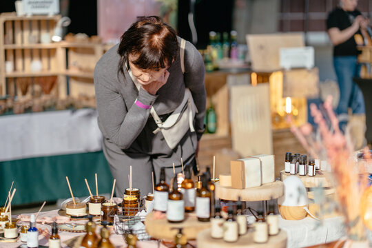 Curious caucasian woman in her 50s smelling candles at handmade market