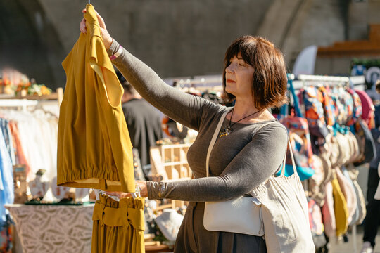 Calm caucasian woman in her 50s choosing yellow dress at street clothing market