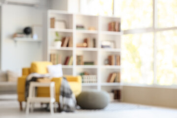 Blurred view of stylish living room with yellow armchair, pouf and bookshelf © Pixel-Shot
