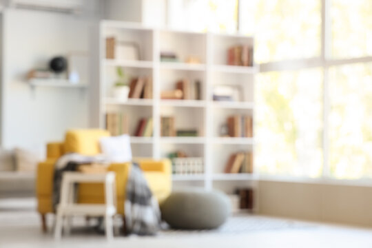 Blurred view of stylish living room with yellow armchair, pouf and bookshelf