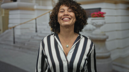 Fototapeta premium Woman in striped shirt wearing gold pendant smiling with finger pointing to head on street; idea happiness.