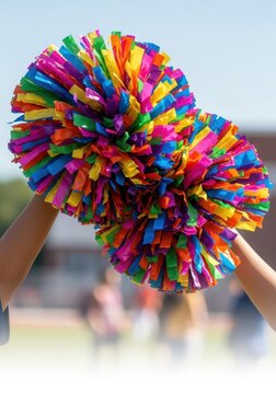 Bright colorful pom-poms are held high and shaken enthusiastically during a school sporting event or high-energy competitive performance, game, sport, poms
