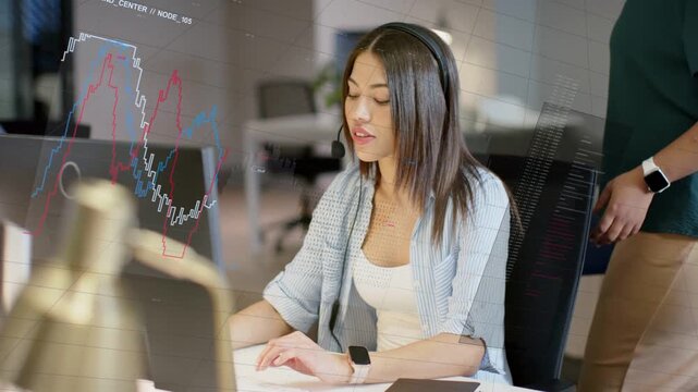 Seated support rep headset on, typing, mouse click showing charts on monitor to help, peer watching