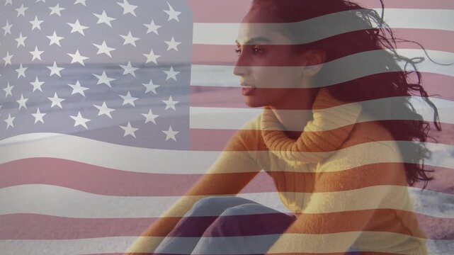 Woman sitting beach turning as breeze lifting hair and US-flag overlay waving, evoking patriotism